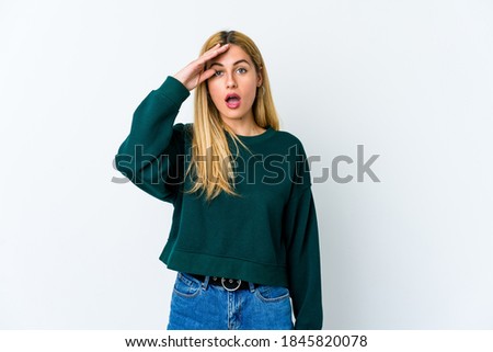 Young blonde woman isolated on white background shouts loud, keeps eyes opened and hands tense.