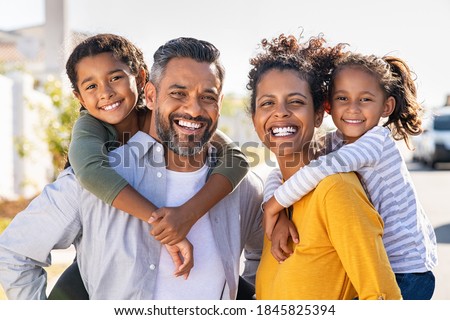 Mixed race parents giving piggyback ride to their children. Portrait of happy african mother and indian father with daughters looking at camera. Smiling family standing with their little girls. Royalty-Free Stock Photo #1845825394