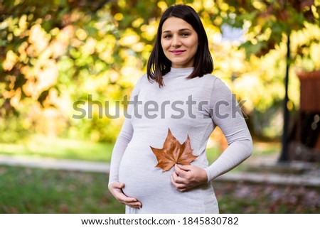 Portrait of happy pregnant woman in park in autumn.