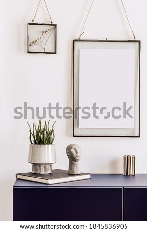 Stylish living room interior with mock up poster frames, navy blue commode, book, decoration and elegant personal accessories in modern home decor.  White wall. Template.