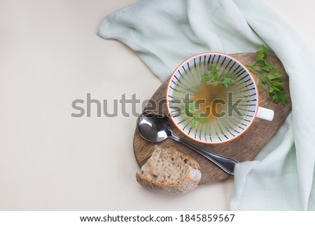 hot meat broth in a white soup cup served with sourdough bread, parsley on a wooden board on white background