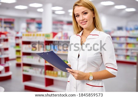 blonde druggist woman in uniform checking the assortment stock in pharmacy, read indications