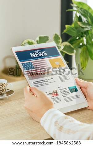 Stock photo of a woman reading news in a website on her tablet in the living room. Concept of online information and reading newspapers on the internet. All contents are composed