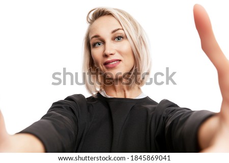 Smiling young blonde woman in black suit photographs herself on the phone. Isolated on a white background. Close-up.