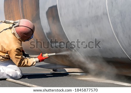 The sandblaster is sanding to steel pipe material. Abrasive blasting, more commonly known as sandblasting, is the operation of forcibly propelling a stream of abrasive material against a surface .