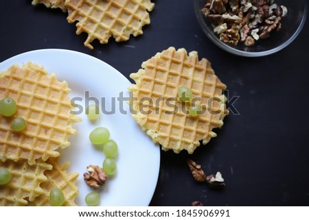 crispy sweet waffles for breakfast on a white plate and a dark background next to fruits grapes and walnuts. for cafe menu signage labels splash screens banners