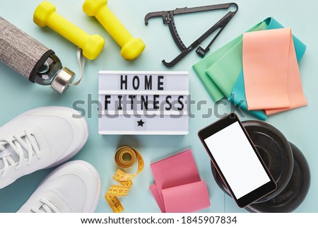 Women's white sneakers, Lightbox with sports slogan, bottle of water, dumbbells, smartphone, measuring tape, caliper and rubber fitness bands. Creative flat lay of sport and fitness equipments.