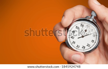 Male hand holding analogue stopwatch on colored background.
