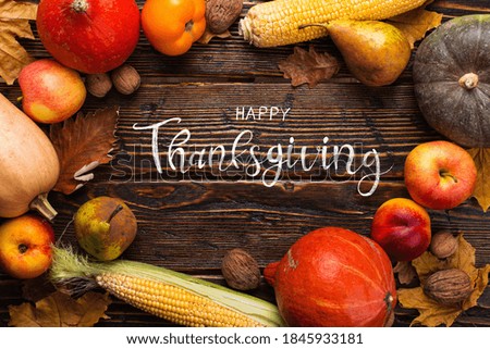Thanksgiving greetings. Pumpkins, vegetables, nuts, dry leaves on wooden background, top view. Kaligraphic capital inscription.