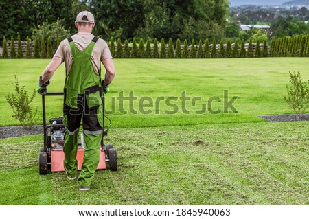 Caucasian Gardener in His 40s and His Powerful Gasoline Lawn Aerator Job For Controlling Lawn Thatch, And Reducing Soil Compaction. Garden Technologies. Royalty-Free Stock Photo #1845940063