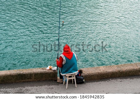 grandmother in a red scarf and blue quilted jacket is fishing waiting for a big fish. active life concept for retirees