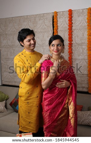 Indian man tying or presenting gold necklace to his beautiful wife on birthday, valentine's day, anniversary or Diwali festival.
