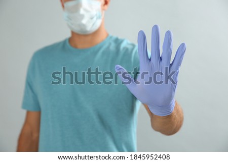 Man in protective face mask and medical gloves showing stop gesture on grey background, closeup