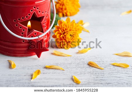 Lit aroma red candle and orange flowers on rustic background. Greeting card for celebration