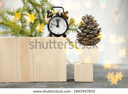 minimal style christmas decor. alarm clock on a podium and fir tree branch with pine cone. simple style home decor. christmas and winter season holiday house decoration. star shaped bokeh. copy space