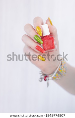 Woman hand with long nails and multi-colored manicure, bottles of nail polishes