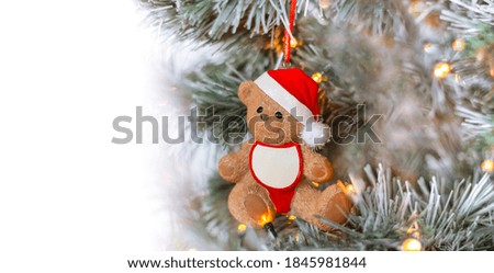 Toy bear in Santa hat on decorated Christmas tree. Winter holiday banner with copy space
