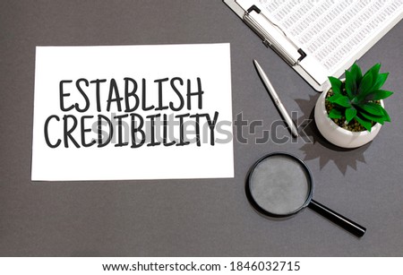 Top view of magnifying glass,calculator,pen, plant and notebook written with ESTABLISH CREDIBILTY sign