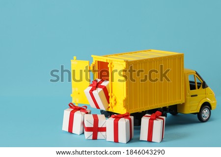 Yellow toy truck delivering gift box on blue background. Cargo transportation, delivery service. Transport company. Infrastructure and logistics. Unloading cardboard box. Copy space