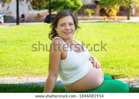 Close up of pregnant belly in nature sitting outdoors on a green grass meadow in a city park on a sunny day