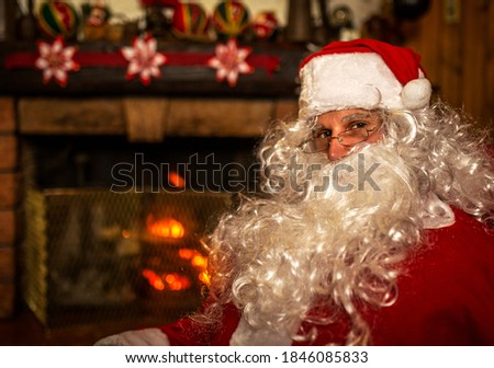 Portrait of Santa claus sitting in the armchair of his house.  Fireplace background on