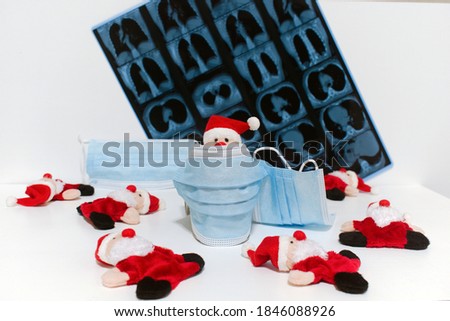 funny santa claus toy hiding behind an antivirus protective medical mask on blurred background x-ray of lungs and fallen other toys Royalty-Free Stock Photo #1846088926