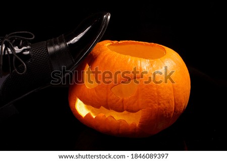 Luxury dark leather male shoe kicking halloween pumpkin on the dark background. Concept of hate Halloween