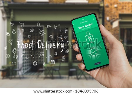 Take away ordering food online from home on moblie device app, food delivery on the way, with word writing Food Delivery and icons app hologram symbols concept, shop front background