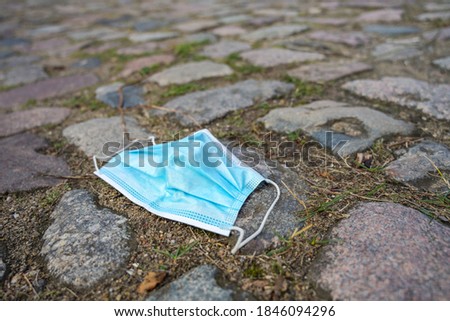 Thrown away surgical face mask against infection with coronavirus and covid-19 on cobblestones, copy space, selected focus, very narrow depth of field Royalty-Free Stock Photo #1846094296