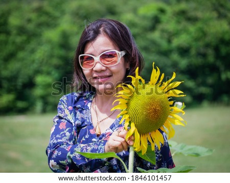 A woman asian​ in a blue dress standing in the field and holding a sunflower