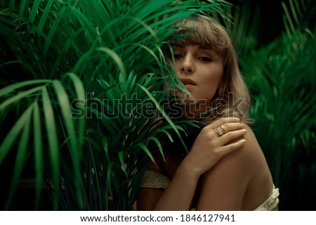 Woman in palm leaves. Model's face in green. Fashion photo of a girl in the tropics