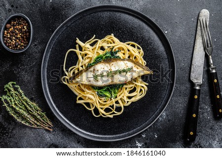 Spaghetti pasta with Halibut fish steak and spinach. Black background. Top view