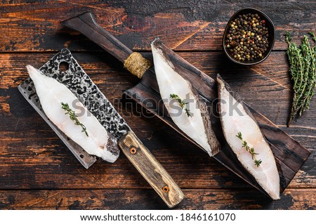 Raw fresh halibut fish steak on a wooden cutiing board. Black background. Top view