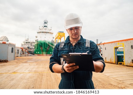 Marine Deck Officer or Chief mate on deck of offshore vessel or ship doing check and filling checklist. Paperwork at sea. Ship is on background Royalty-Free Stock Photo #1846169413