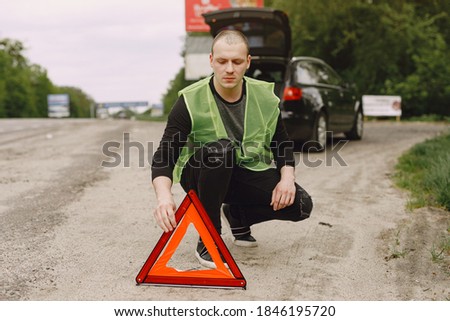 Driver putting warning triangle on asphalt road. Emergency stop concept.