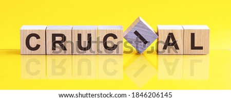 CRUCIAL word written on wood block. CRUCIAL word is made of wooden building blocks lying on the yellow table. CRUCIAL, business concept, yellow background