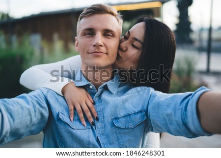 Selfie portrait of Caucasian boyfriend looking at camera while girlfriend kissing him in cheek enjoying together recreation, close up of couple in love posing for shooting romantic video content