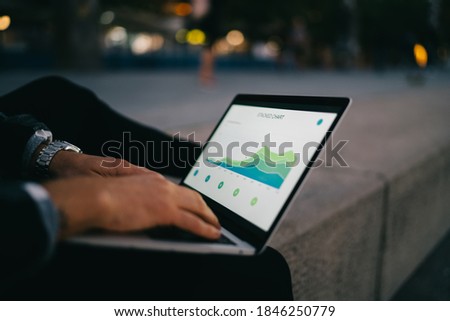 Cropped image of male digital nomad browsing financial news from exchange working on freelance, man student learning online course keyboarding on laptop computer checking graphic charts on web page