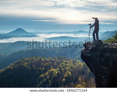 Professional on cliff. Nature photographer hold tripod with camera. Man at sunrise at open view on mountain peak