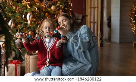 Wide banner panoramic view of happy young Caucasian mother and little daughter do Christmas tree decoration together. Smiling caring mom and small girl child decorate fir tree on winter holidays.