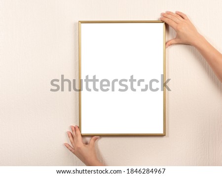 Young woman holding empty picture frame with copyspace in vertical position. hanging a photo frame mockup on a white wall. Picture frame mockup