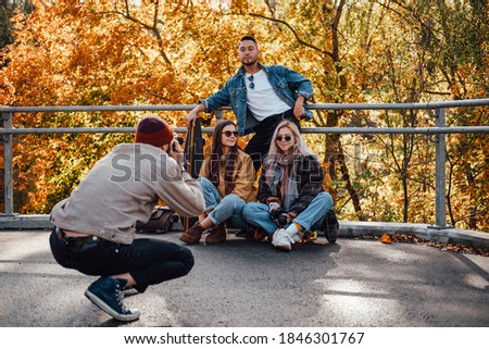 Professional photographer taking picture of his friends they are posing in autumn landscape background in daytime.