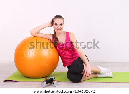 Young beautiful fitness girl exercising with orange ball and dumbbells in gym