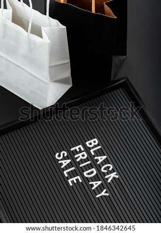 Black Friday sale text on black Letter Board with shopping paper bags on black background. Delivery black and white craft paper bag package