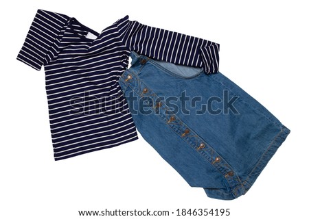 Closeup of folded cute sleeveless blue denim overall dress and striped t-shirt for little child girl isolated on a white background. Jeans fashion for kids.