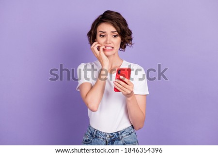 Photo portrait of nervous worried girl with bob hair looking at mobile phone biting fingers isolated on vibrant purple color background