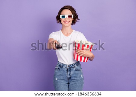 Photo portrait of girl smiling holding pop-corn box wearing 3d glasses holding remote controller isolated on vibrant purple color background