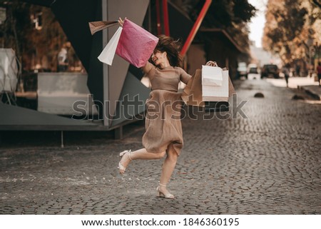 Young very happy woman in a dress and gift bags walking in the city, jumping, shopping, having fun. 