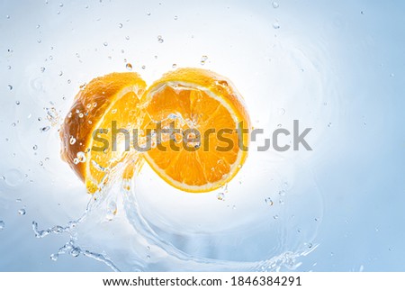 Two halves of orange fruit splashing into clear water, isolated on light blue background. Health food concept