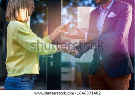 The real estate agent gives the man the key to the new apartment. A couple of people are standing in front of a modern building, the woman is holding a key to a new apartment.
